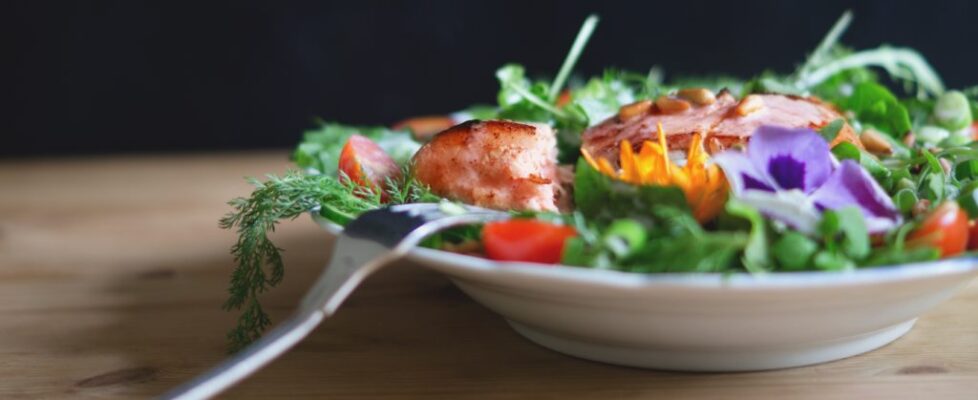 Photo of a salad with salmon served in a white dish.